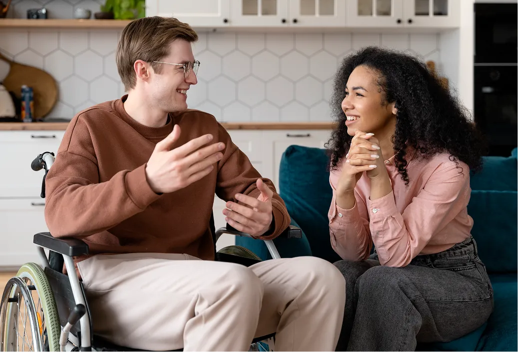 A man using a wheelchair and a support worker share a happy conversation at home
