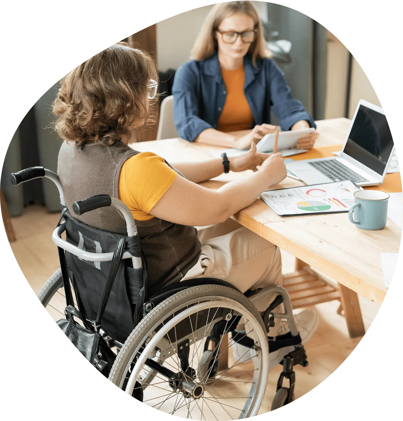 A support worker helps a woman in a wheelchair with documents at a kitchen table