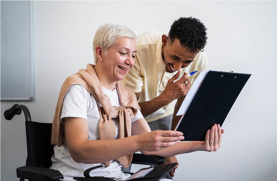 A support worker and a smiling woman in a wheelchair review paperwork together