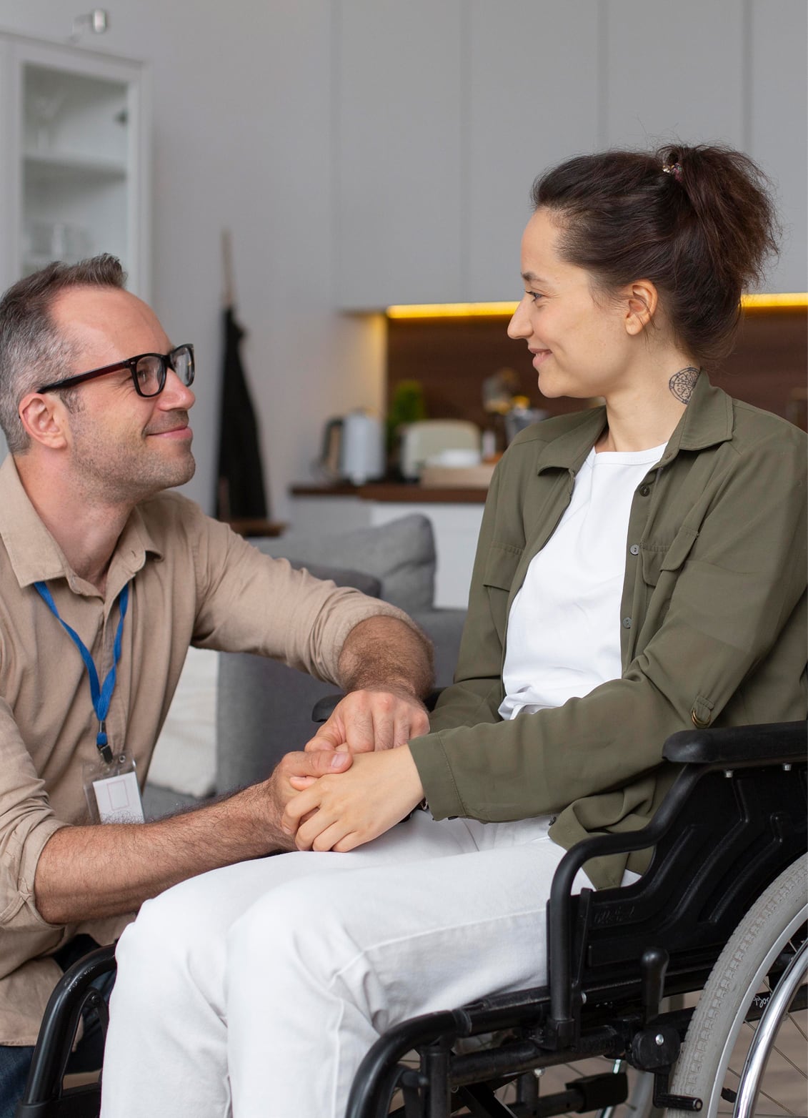 A support worker holds hands with a woman in a wheelchair during a home visit