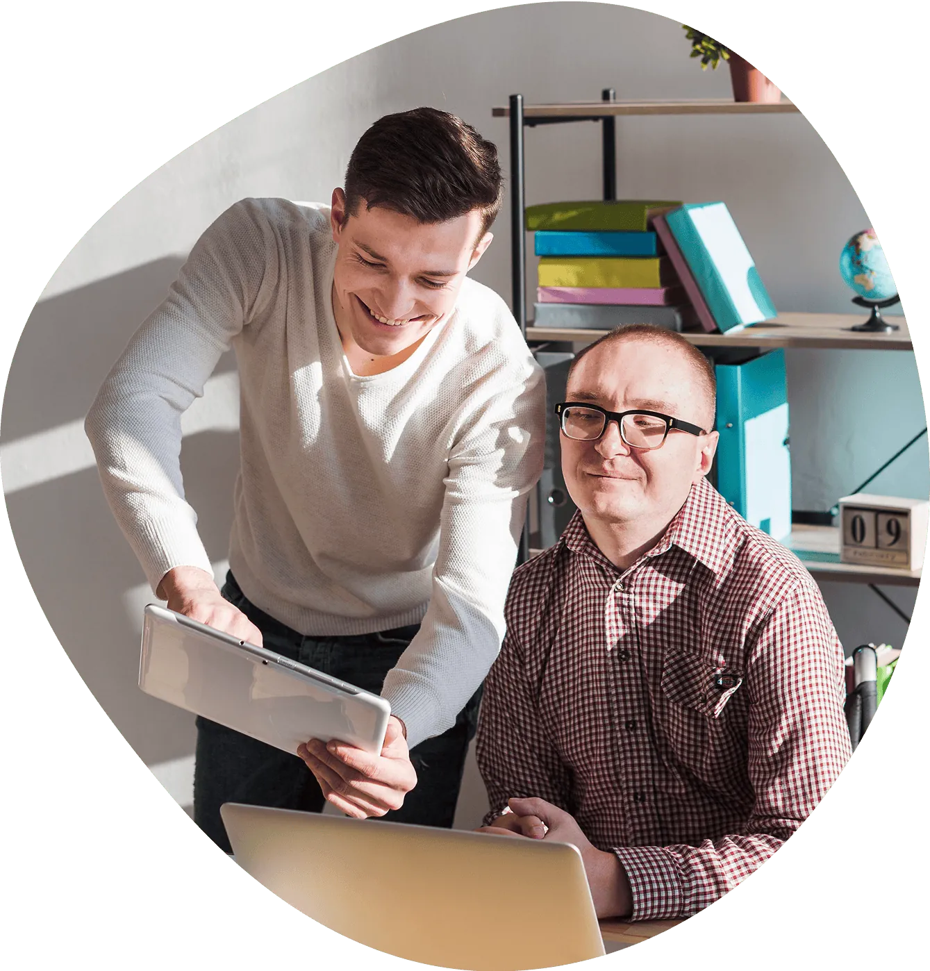 A support worker shares a tablet with a smiling man at a desk